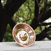 Copper plate with a reflective interior on a stone surface with trees in the background