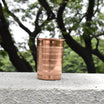Copper tumbler on a concrete surface with trees in the background