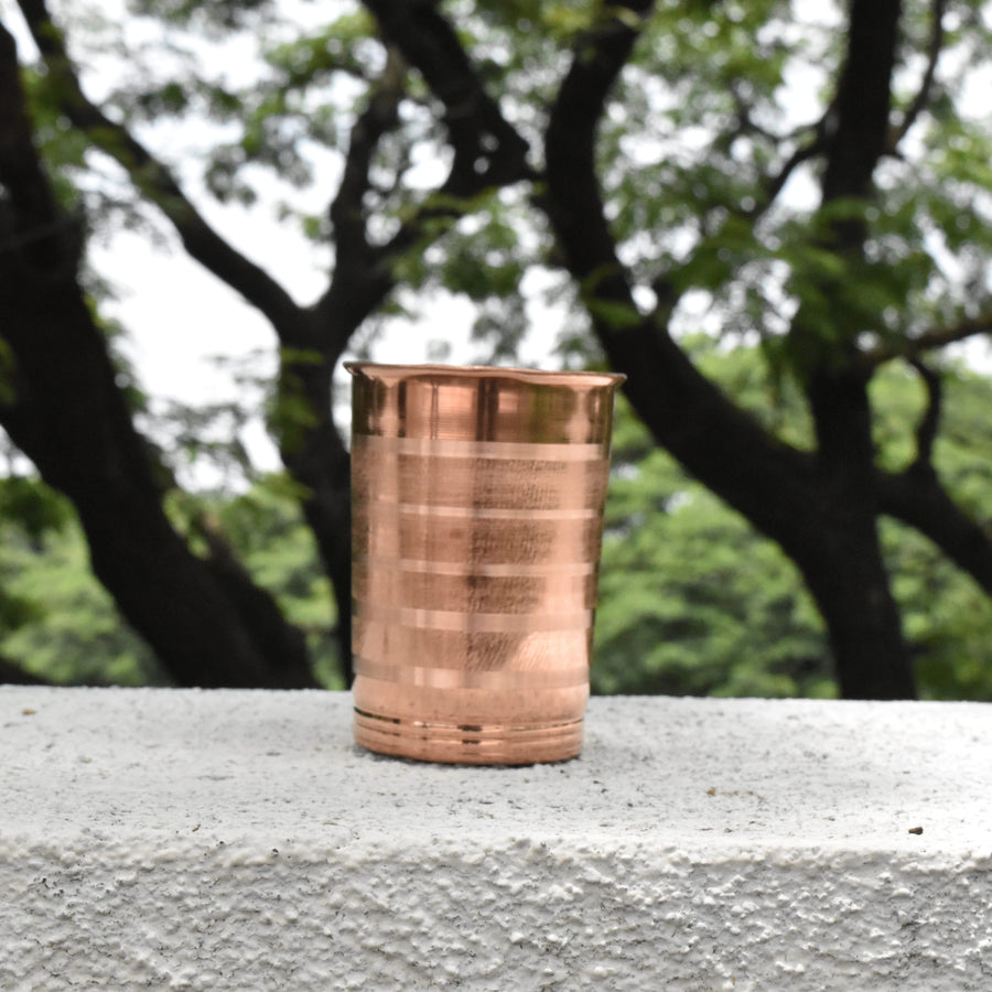Copper tumbler on a concrete surface with trees in the background